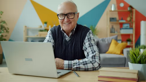 smiling elderly man at desk with laptop